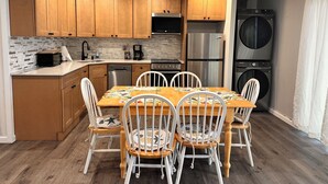 A modern kitchen with wooden cabinets, a stainless steel refrigerator, a dishwasher, and a built-in oven. There is a dining table with white chairs and a colorful tablecloth. - Charming 2-bedroom condo with WiFi, AC in amazing Ocean City (Ocean City)