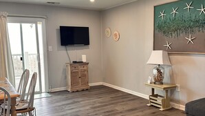 A spacious living room with a wooden floor, a flat-screen TV mounted on the wall, a dining area with chairs and a table, and a large painting of sea stars. - Charming 2-bedroom condo with WiFi, AC in amazing Ocean City (Ocean City)