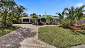 A single-story house with a green metal roof, surrounded by a well-maintained lawn and palm trees. - Welcome To The Leaf House (Delray Beach)