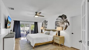 A bedroom with a bed, nightstands, a ceiling fan, a TV, and a view of the outdoors. - Welcome To The Leaf House (Delray Beach)