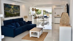 A modern living room with a dark blue sofa, a wooden coffee table, and a large painting on the wall. - NEW apt. 1 min. walk from beach, sea view, large terrace, two pools (Albufeira)