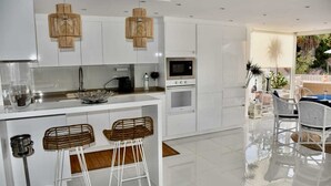 A modern kitchen with white cabinetry, a central island with bar stools, a microwave, an oven, and a hanging light fixture. - NEW apt. 1 min. walk from beach, sea view, large terrace, two pools (Albufeira)