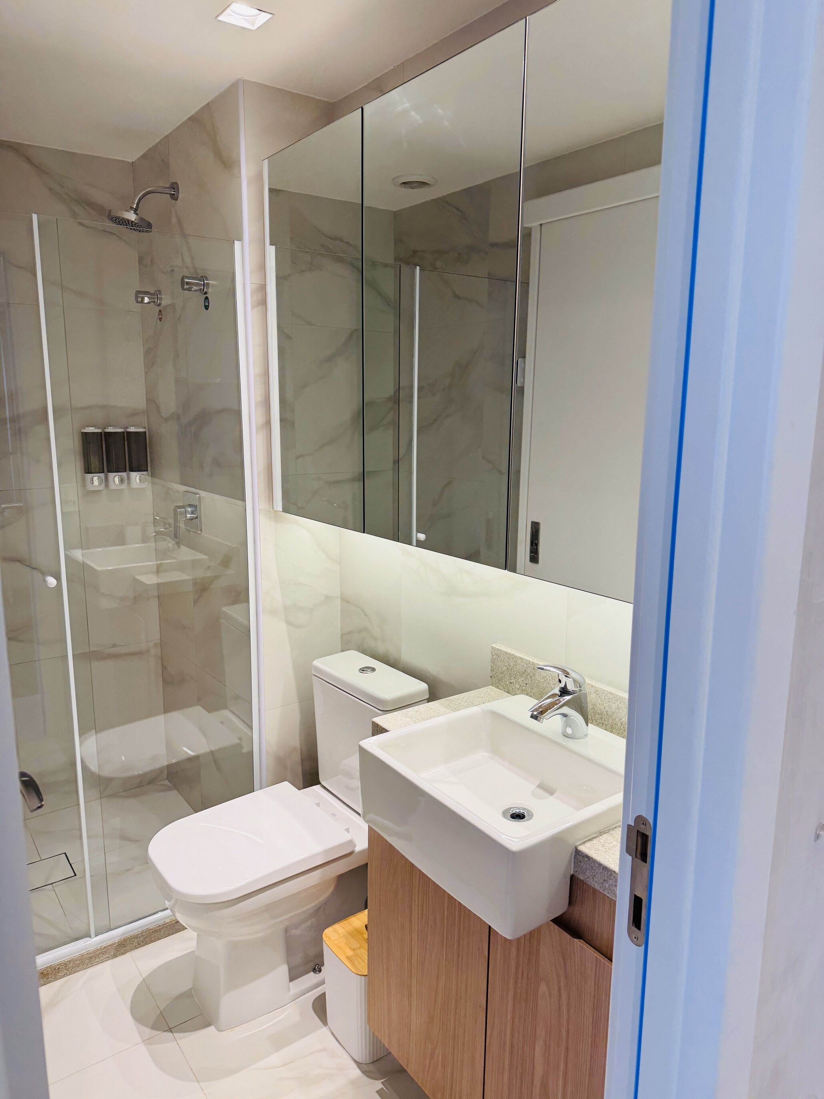 Un baño moderno con ducha envuelta en vidrio, inodoro blanco y tocador de madera con lavamanos.