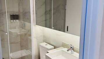 Un baño moderno con ducha envuelta en vidrio, inodoro blanco y tocador de madera con lavamanos.