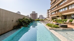 Piscina no terraço com piso em azulejo, espreguiçadeiras e plantas em vasos.