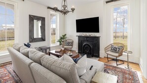 A living room with a sofa, a fireplace, a television, and a large window. - Historic Home & Farm in Bourbon Country  (Warsaw)