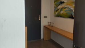 A hallway with a dark door, a wooden bench, and a colorful abstract painting on the wall.