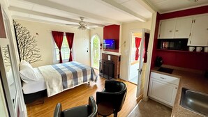 Una camera compatta con un letto, una scrivania, una sedia, angolo cottura e ventilatore a soffitto.