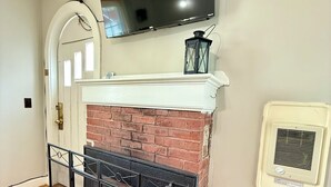 A room with a fireplace, a television mounted above it, and a wall-mounted air conditioning unit. - Bar Harbor Cottage Close to Acadia & Downtown Bar Harbor - Kitchen, AC, Wi-Fi, Fireplace (Sleeps 6). (Bar Harbor)