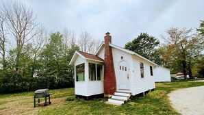 A small white house with a brick chimney, a porch, and a garage. - Bar Harbor Cottage Close to Acadia & Downtown Bar Harbor - Kitchen, AC, Wi-Fi, Fireplace (Sleeps 6). (Bar Harbor)