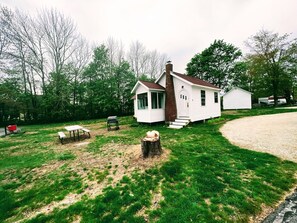 Ein kleines weißes Haus mit Schornstein, einer Veranda und einem Hof mit Picknicktisch und Grill.