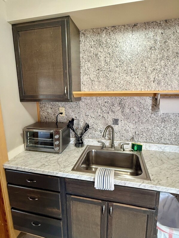 A kitchen with dark cabinets, a granite countertop, a stainless steel sink, and a built-in toaster.