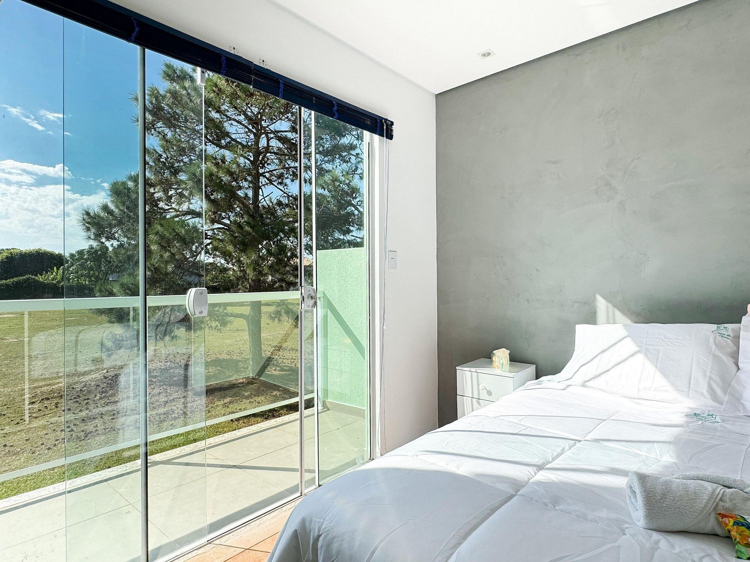 A bedroom with a large sliding glass door leading to a balcony, a bed with white bedding, and a nightstand with a lamp.