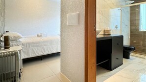 A modern hotel room with a bed, a radiator, a wooden door, and a bathroom with a shower and a toilet.