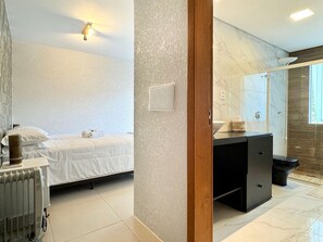 A modern hotel room with a bed, a radiator, a wooden door, and a bathroom with a shower and a toilet.