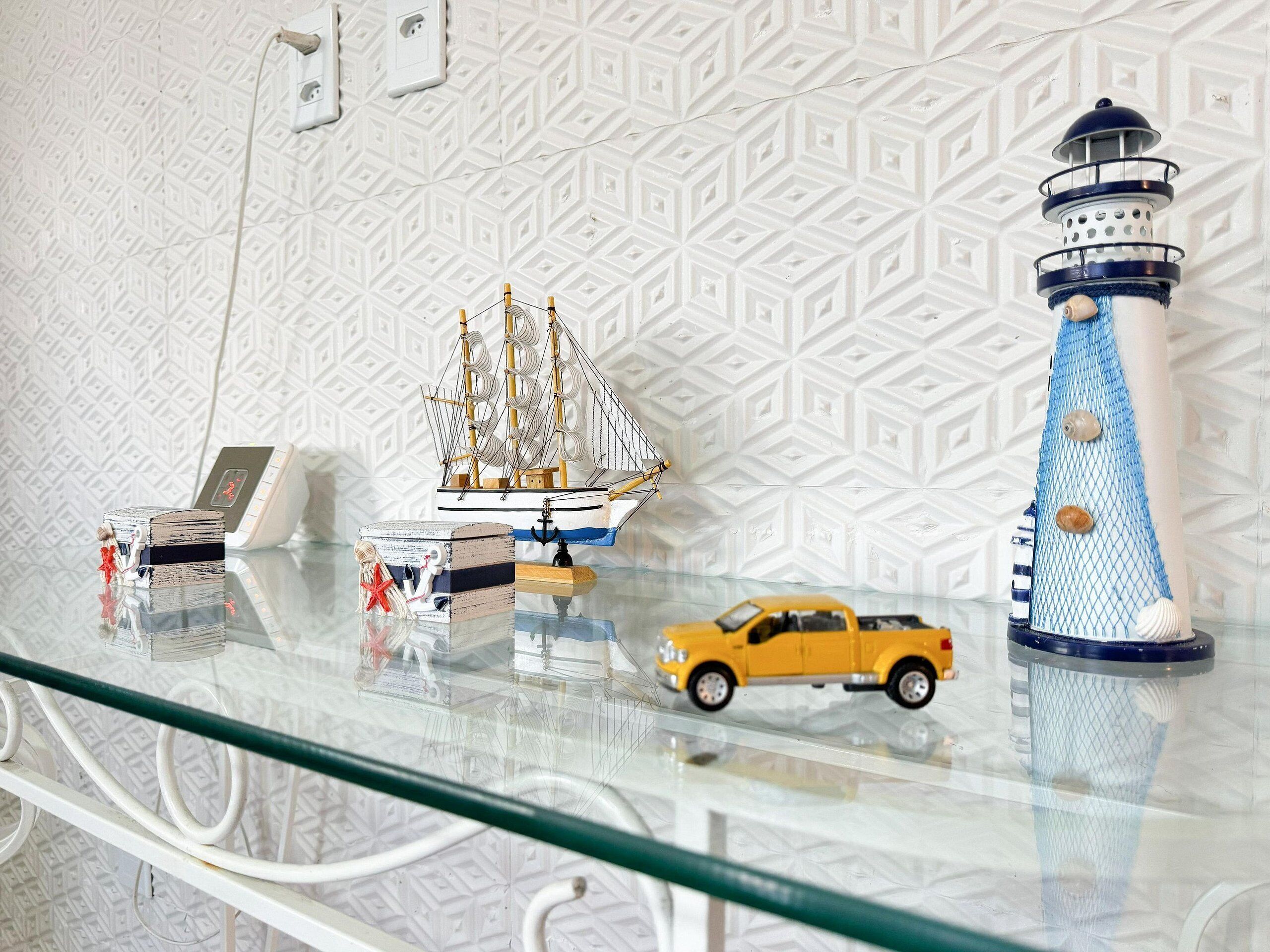 A glass display table with a model ship, a lighthouse, a telephone, and a car.