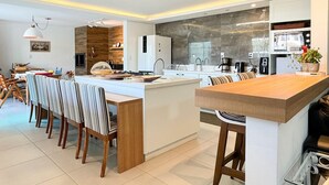 A modern kitchen with a central island, white cabinetry, and a dining area with striped chairs.