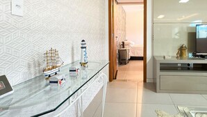 A modern room with a glass table displaying model ships and a lighthouse, a television on a cabinet, and a door leading to another room.