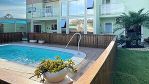 A two-story building with a swimming pool, wooden deck, and a small garden area. - Casa de Andréa com piscina - Campeche (Florianopolis)