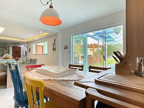 A dining area with a wooden table and chairs, a hanging light fixture, and a view of a backyard through glass doors.