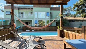 A wooden deck with a pool, lounge chairs, and a hammock. - Casa de Andréa com piscina - Campeche (Florianopolis)