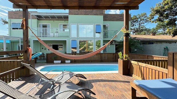 A wooden deck with a pool, lounge chairs, and a hammock.