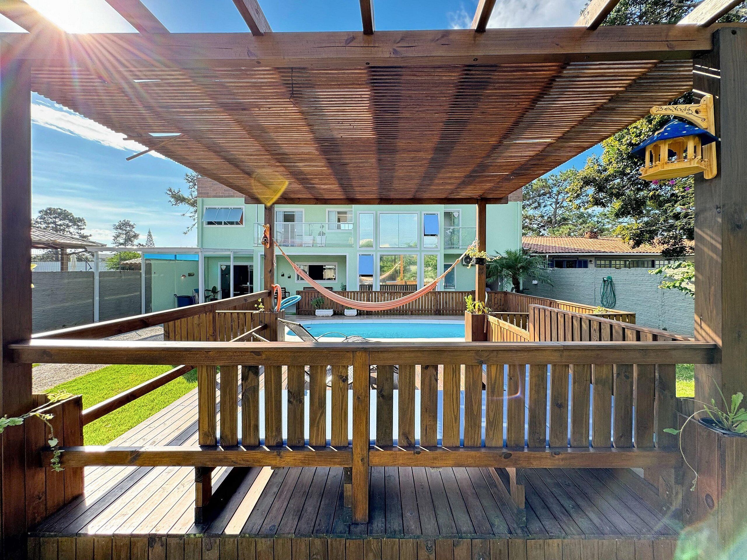 A wooden deck with a hammock, a pool, and a view of a two-story building.