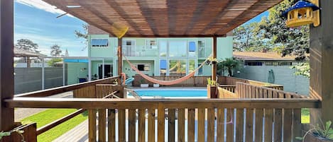 A wooden deck with a hammock, a pool, and a view of a two-story building.