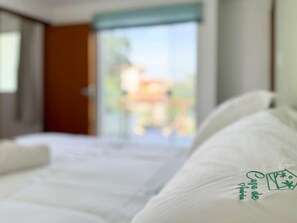 Une chambre d’hôtel avec un lit, une fenêtre donnant sur un espace verdoyant et une porte.