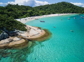 Une plage côtière aux eaux turquoise et limpides, bordée de formations rocheuses et d’une végétation luxuriante.