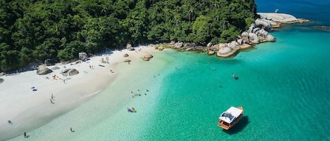 Vista aérea de una playa con aguas turquesas cristalinas, una orilla arenosa y un promontorio cubierto de bosque.