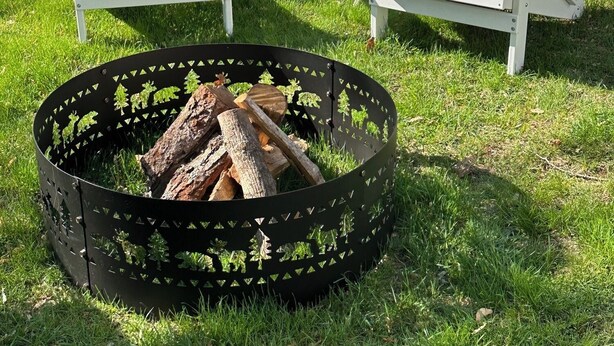 Två vita Adirondack-stolar och en svart metallringad eldstad med ved.