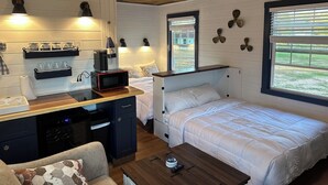 A compact room with a kitchenette, a bed, a small seating area, and a window with blinds. - Cozy studio cottage in Bar Harbor - Kitchen, AC, Wi-Fi & Fireplace (Bar Harbor)
