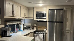 A modern kitchen with wooden cabinets, a stainless steel refrigerator, a microwave, an oven, and a coffee maker. - Cozy campground with WiFi and AC.  Walk to the Charlotte motor speedway. (Concord)
