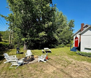 A backyard with a fire pit, outdoor seating, a red door, and a white building.
