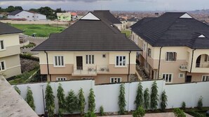 Una hilera de edificios residenciales con techos planos y balcones, rodeados de vegetación y un cielo nublado.