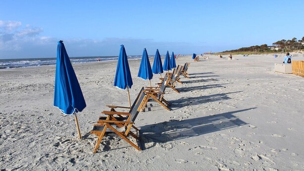 A beach with rows of blue umbrellas and wooden beach chairs. - Forest Beach Villas - 5 Min. Walk to Coligny Beach (Hilton Head Island)