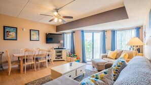 A living room with a sofa, coffee table, and dining area with chairs and a TV. - Forest Beach Villas - 5 Min. Walk to Coligny Beach (Hilton Head Island)