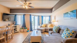 A living room with a ceiling fan, a flat-screen TV, a sofa set, a coffee table, and a dining area with chairs and a table. - Forest Beach Villas - 5 Min. Walk to Coligny Beach (Hilton Head Island)