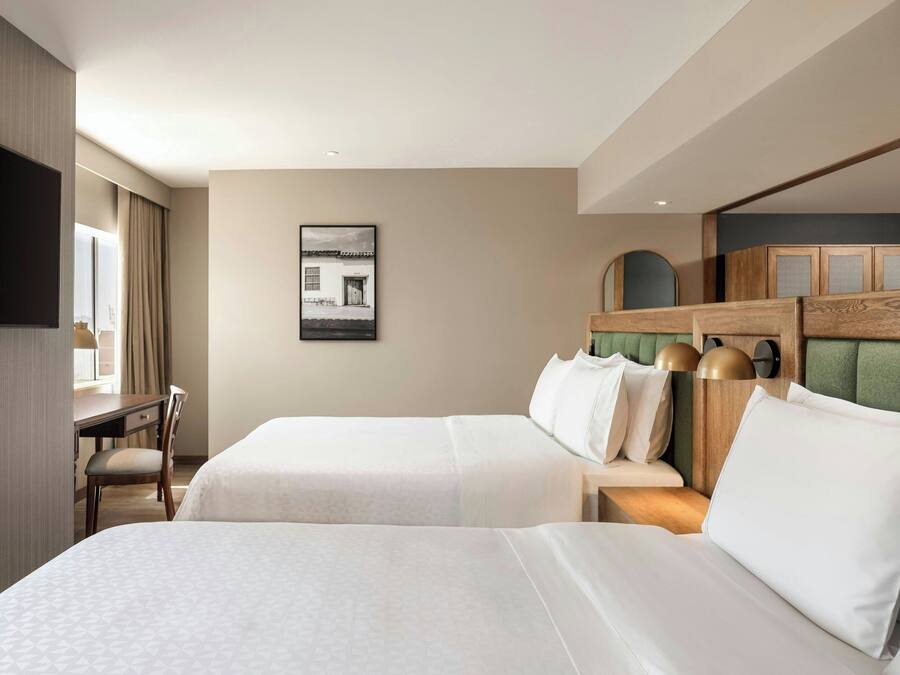 Quarto de hotel com duas camas, uma escrivaninha e uma televisão.
