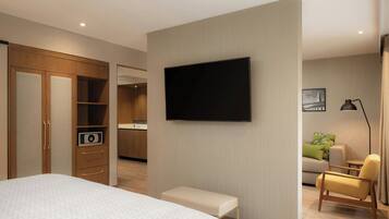 A modern hotel room with a large bed, a TV mounted on the wall, a small bench, a sofa, and a desk with a lamp.