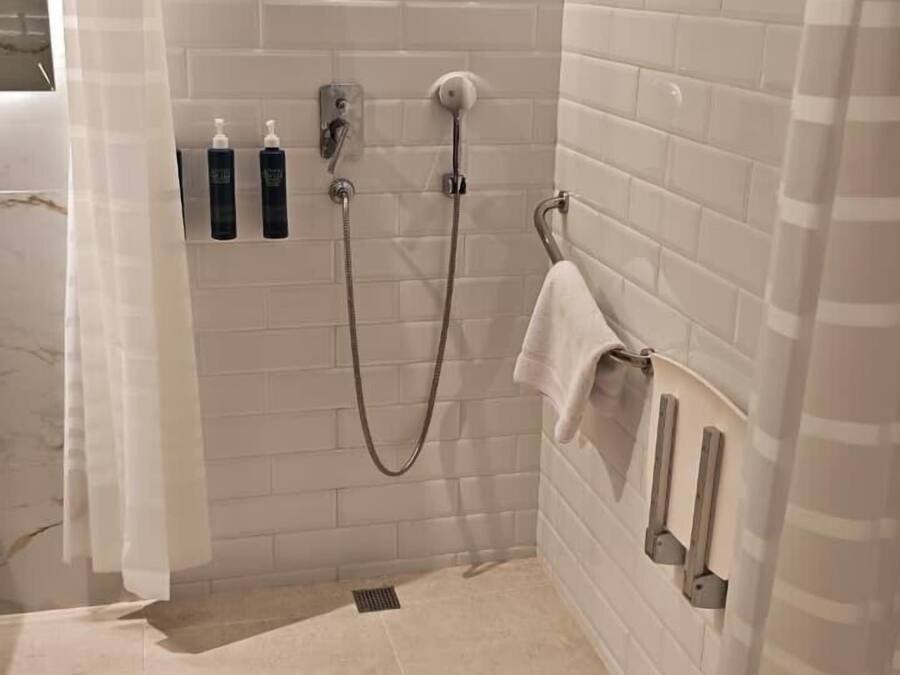 A small, tiled shower area with a handheld showerhead, a towel rack, and two bottles of shampoo.