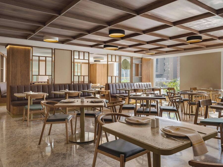 Un interior de restaurante moderno con mobiliario de madera, ventanas amplias y techo a cuadros.