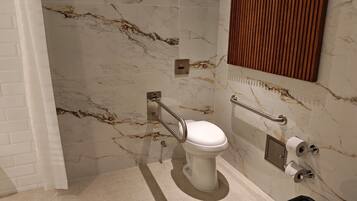 A bathroom with a marble wall, a white toilet, and a wooden panel above the mirror.