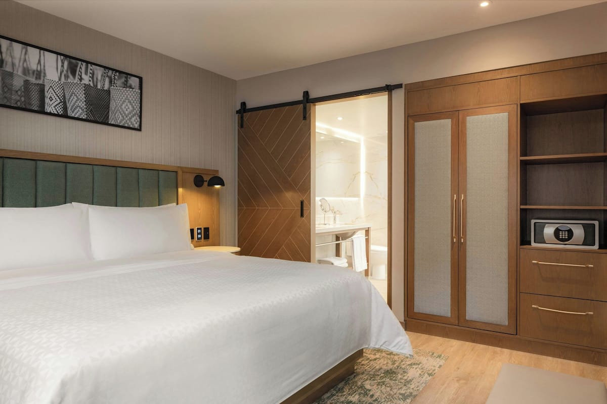 Une chambre d’hôtel avec un grand lit, un placard à portes coulissantes, une table de chevet avec une lampe et une œuvre d’art accrochée au mur.