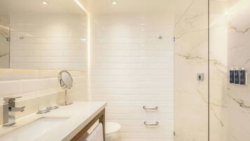 A modern bathroom with a white tiled shower, a glass-enclosed shower, a marble wall, and a vanity with a mirror and sink.