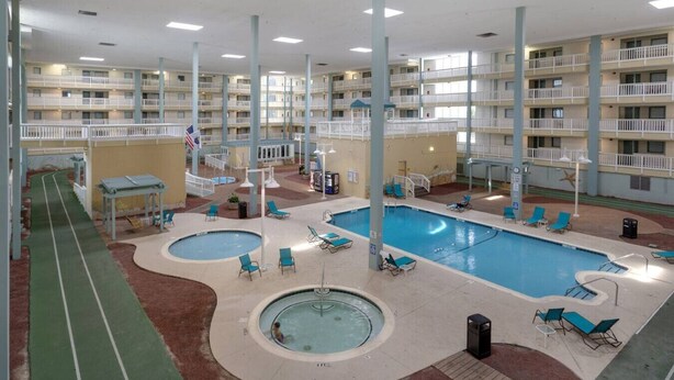 Un hotel con varios pisos, piscinas interiores y una pista de atletismo verde.