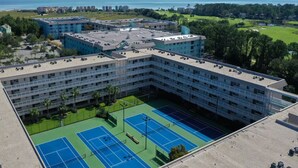 Un hotel de varios pisos con cancha de tenis y vista al mar.