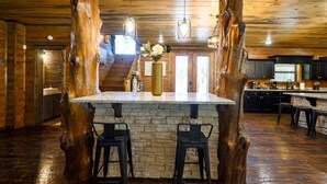 A rustic kitchen with a central island, stone accents, and wooden beams. - Sleeps 24 * Luxe Pool Cabin Secluded w/Game Room (Broken Bow)