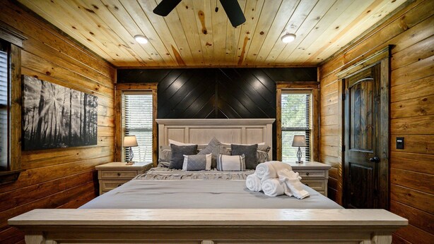 A wooden-paneled bedroom with a large bed, two bedside tables, and a black accent wall. - Sleeps 24 * Luxe Pool Cabin Secluded w/Game Room (Broken Bow)